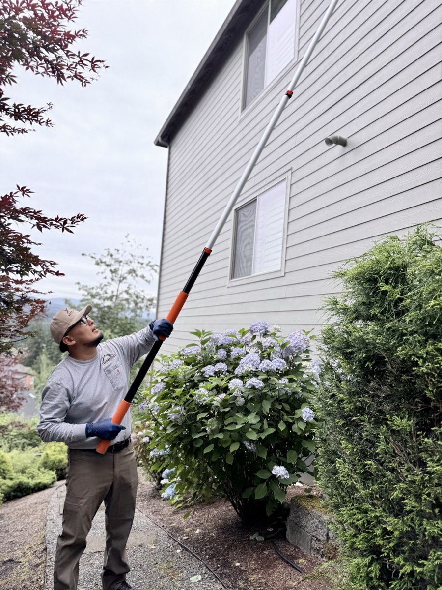 Pest control technician reaching an upper exterior eave